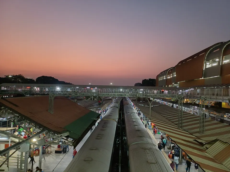Trains standing at the platforms of Pune railway station in the evening, with the foot overbridge and passengers on the platforms