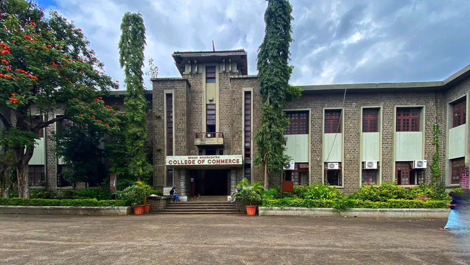 The stone main building of Brihan Maharashtra College of Commerce in Pune, with trees and an open forecourt