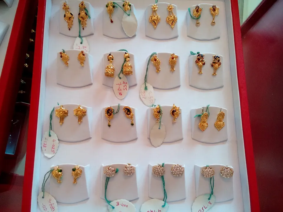 Pairs of gold earrings laid out in a red-and-white display tray at a jeweller’s, each with a small weight tag