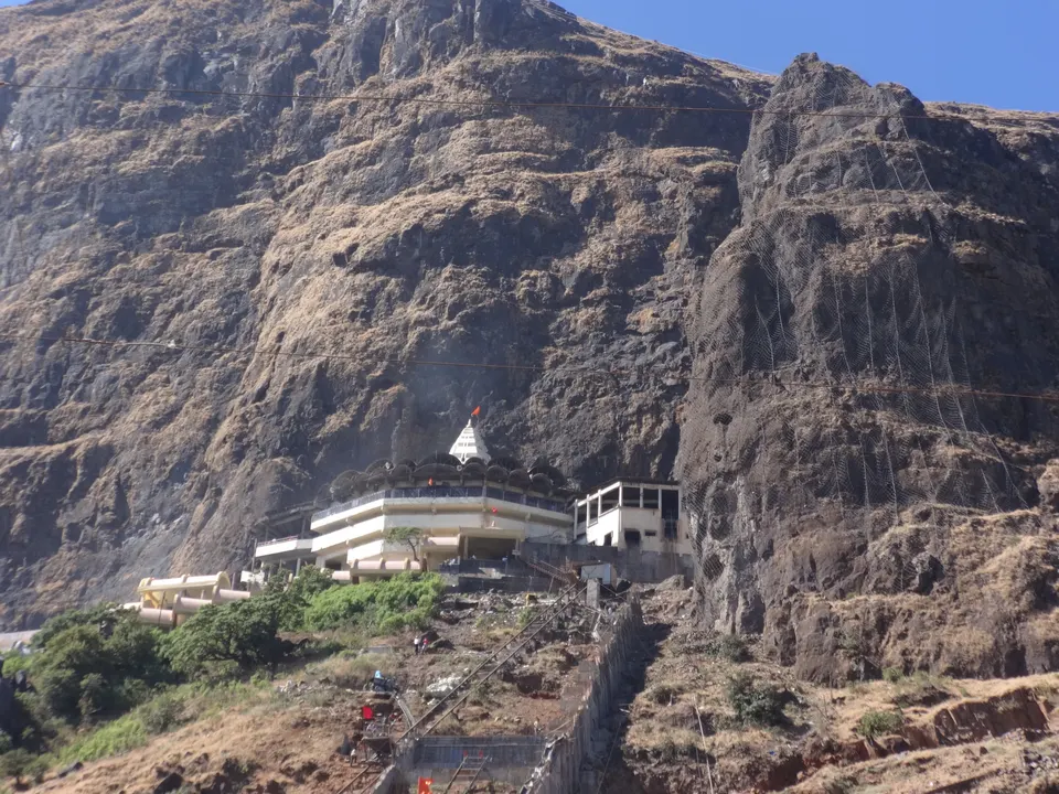 The Saptashrungi Devi temple at the foot of a sheer rock face on Saptashrungi Gad, with a stairway climbing up to it