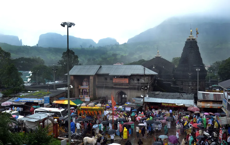 The Trimbakeshwar temple below the Brahmagiri hills, with devotees gathered in the rain on the street in front of it