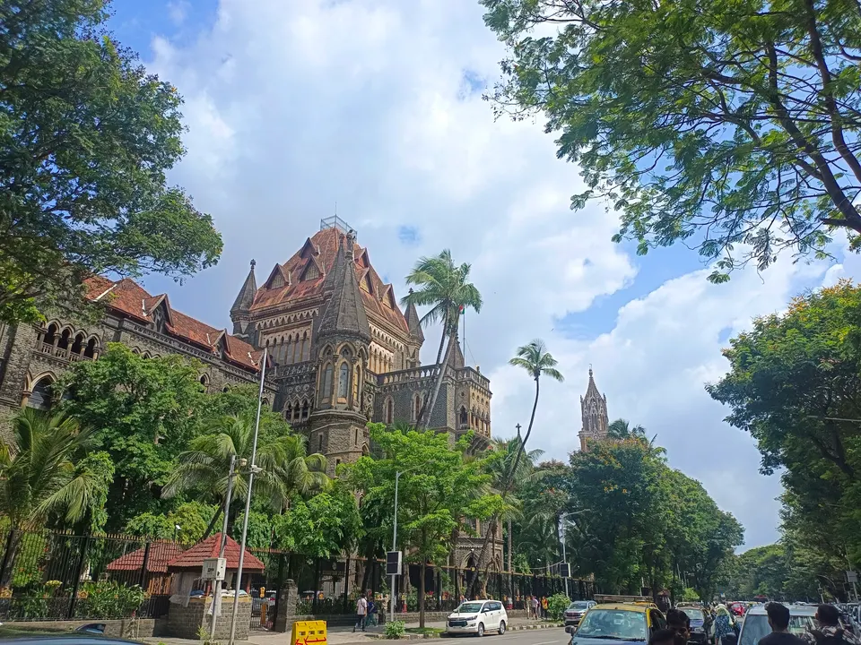 झाडांच्या मधून दिसणारी मुंबई उच्च न्यायालयाची दगडी गॉथिक इमारत आणि समोरचा रस्ता