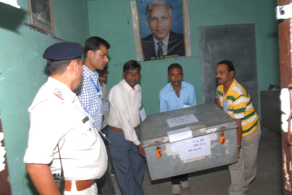 सील केलेली धातूची मतपेटी उचलून नेणारे निवडणूक कर्मचारी, शेजारी उभा पोलीस अधिकारी