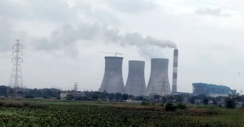 Three cooling towers and a smoking chimney of the Koradi thermal power station seen beyond farmland